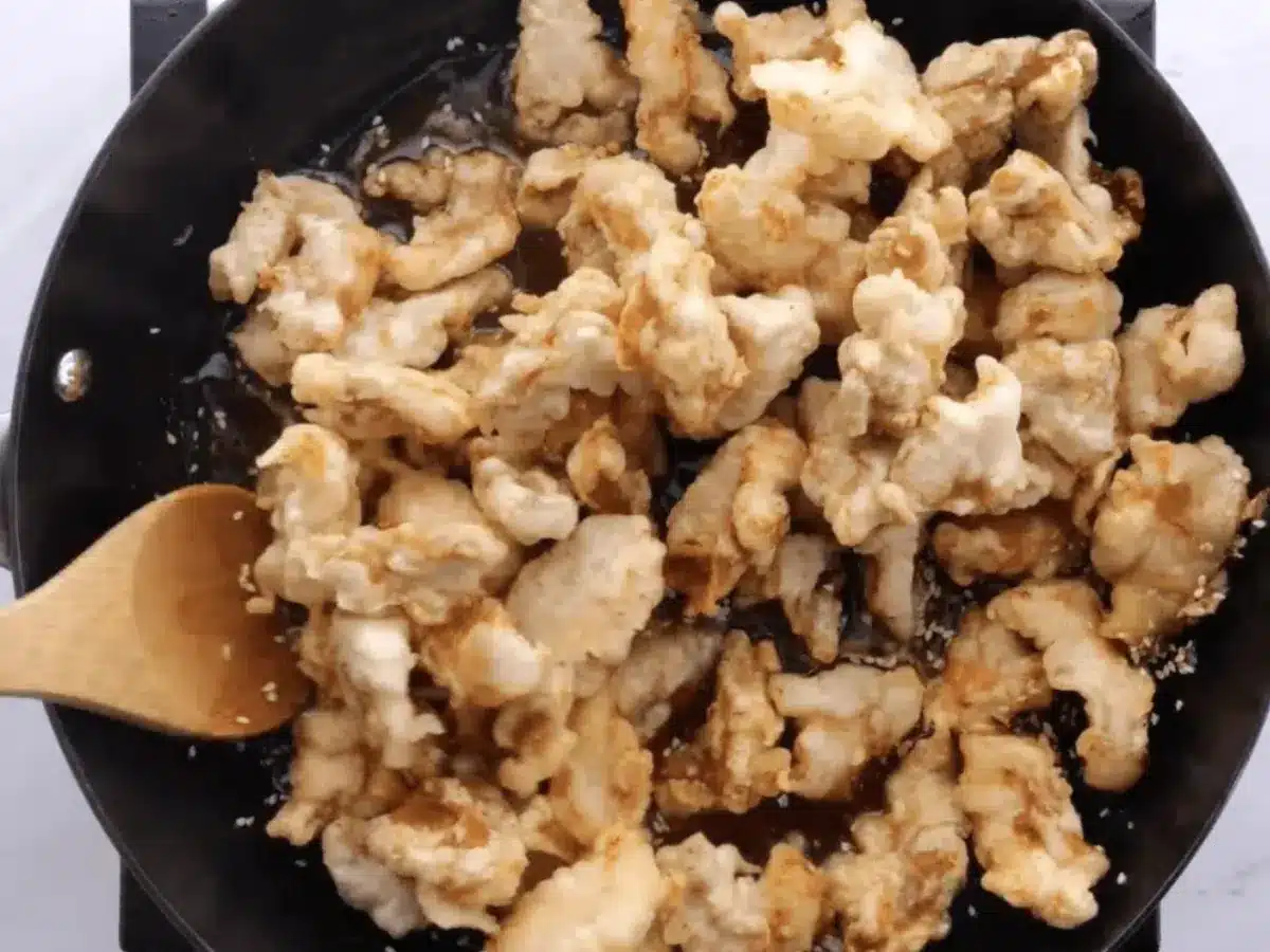 Chicken cooking in pan with wooden spoon