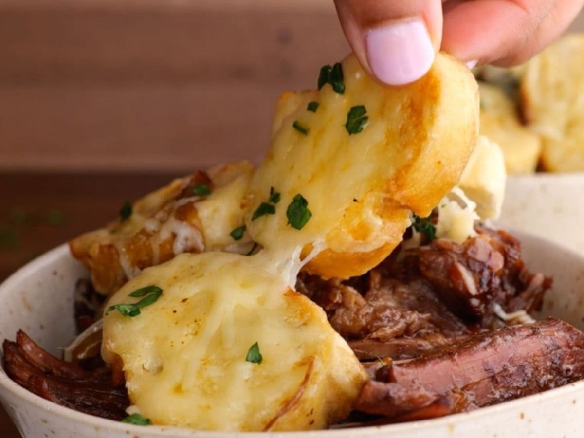 Pulling small piece of toasted bread with cheese from a pot roast