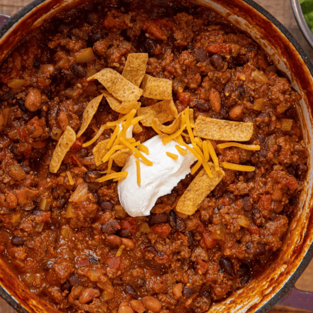 Cooked chili in pot with sour cream, fritos, and cheese on top