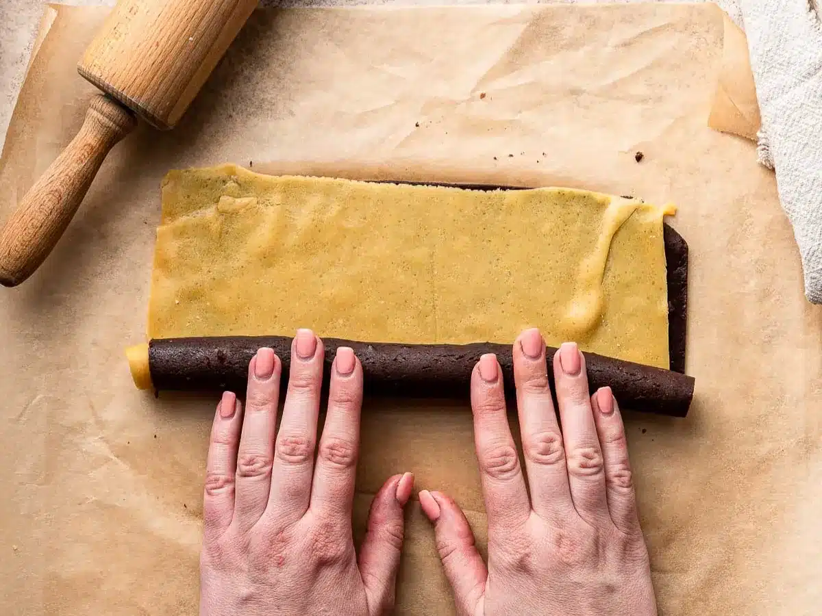 Two different colors of dough cut into rectangles rolled into cylinder.