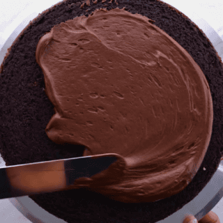 spreading cocoa frosting on top of chocolate cake with spatula