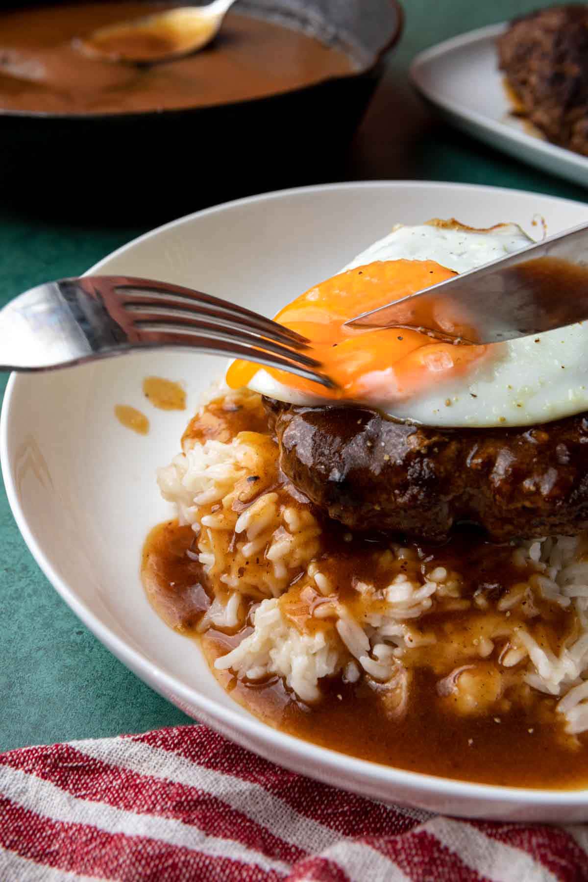 Loco Moco assembled dish on plate, fork and knife cutting egg yolk