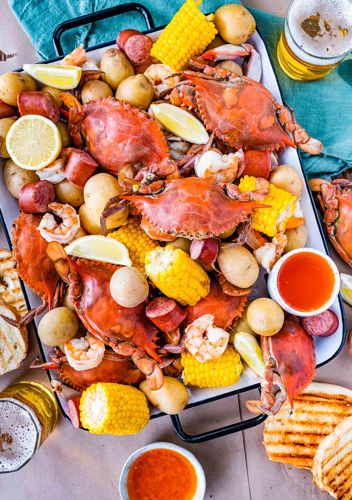 Low Country Boil cooked crab, corn, sausage, and potatoes on platter with toasted bread and melted butter