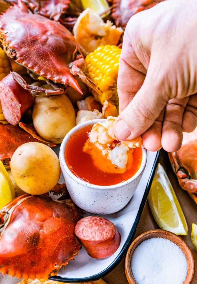 Low Country Boil dipping shrimp in melted butter on platter with the rest of the boil