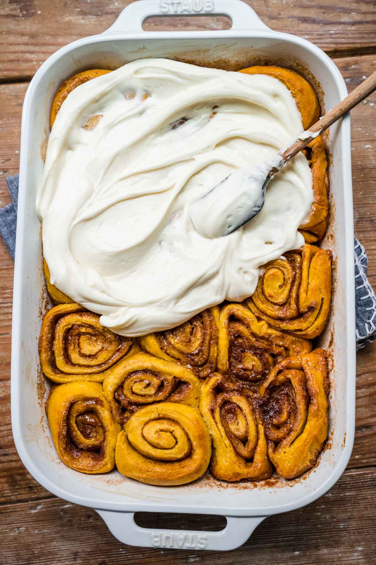 Pumpkin Cinnamon Rolls spreading icing on rolls in baking pan