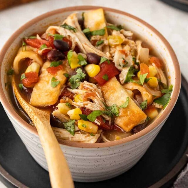 Slow Cooker Chicken Tortilla Soup in bowl with wooden spoon side angle view