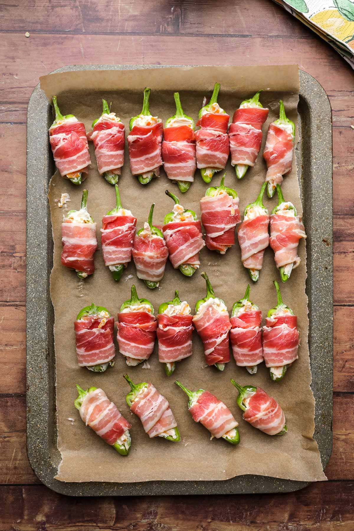 Bacon Jalapeno Poppers raw halved stuffed jalapenos wrapped in bacon on baking sheet