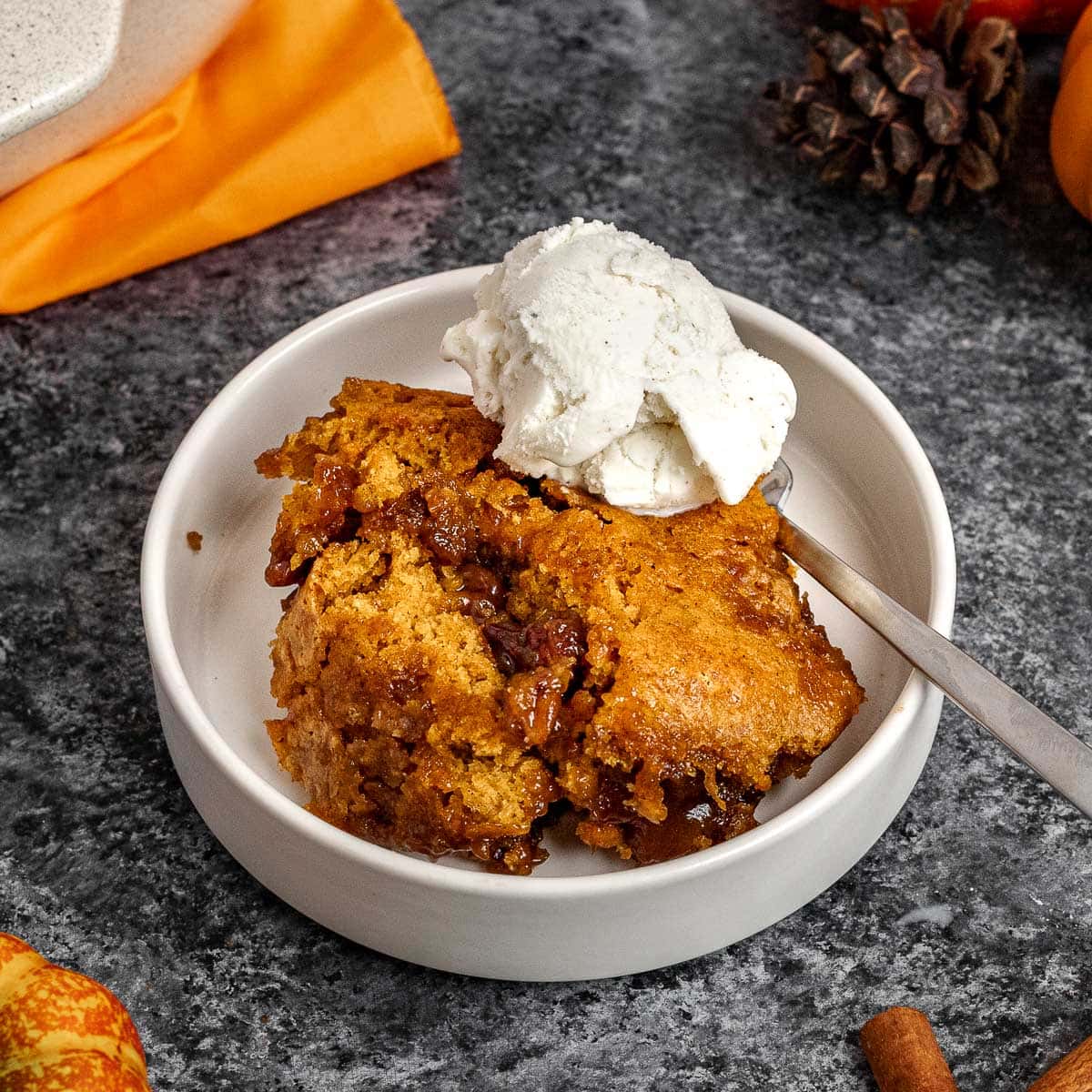 Pumpkin Cobbler slice in bowl with spoon and ice cream on top