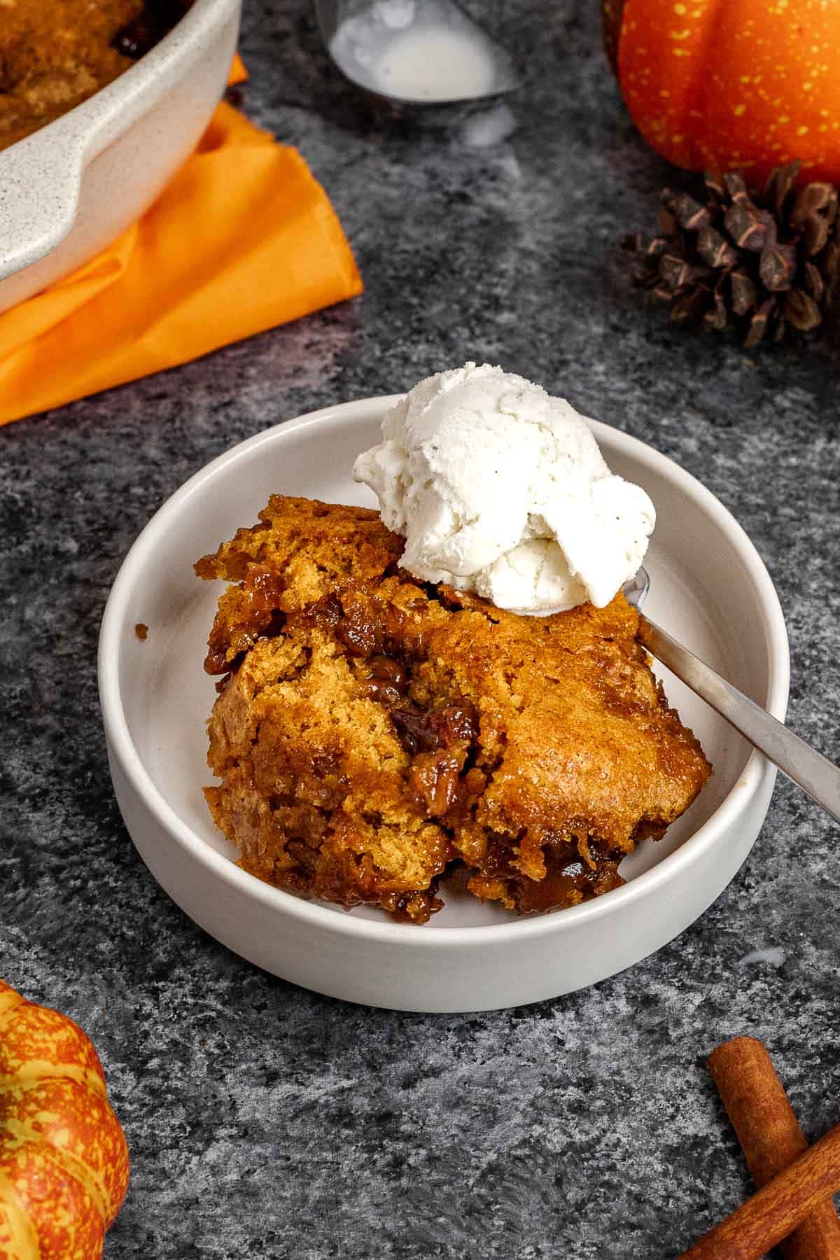 Pumpkin Cobbler slice in bowl with spoon and ice cream on top