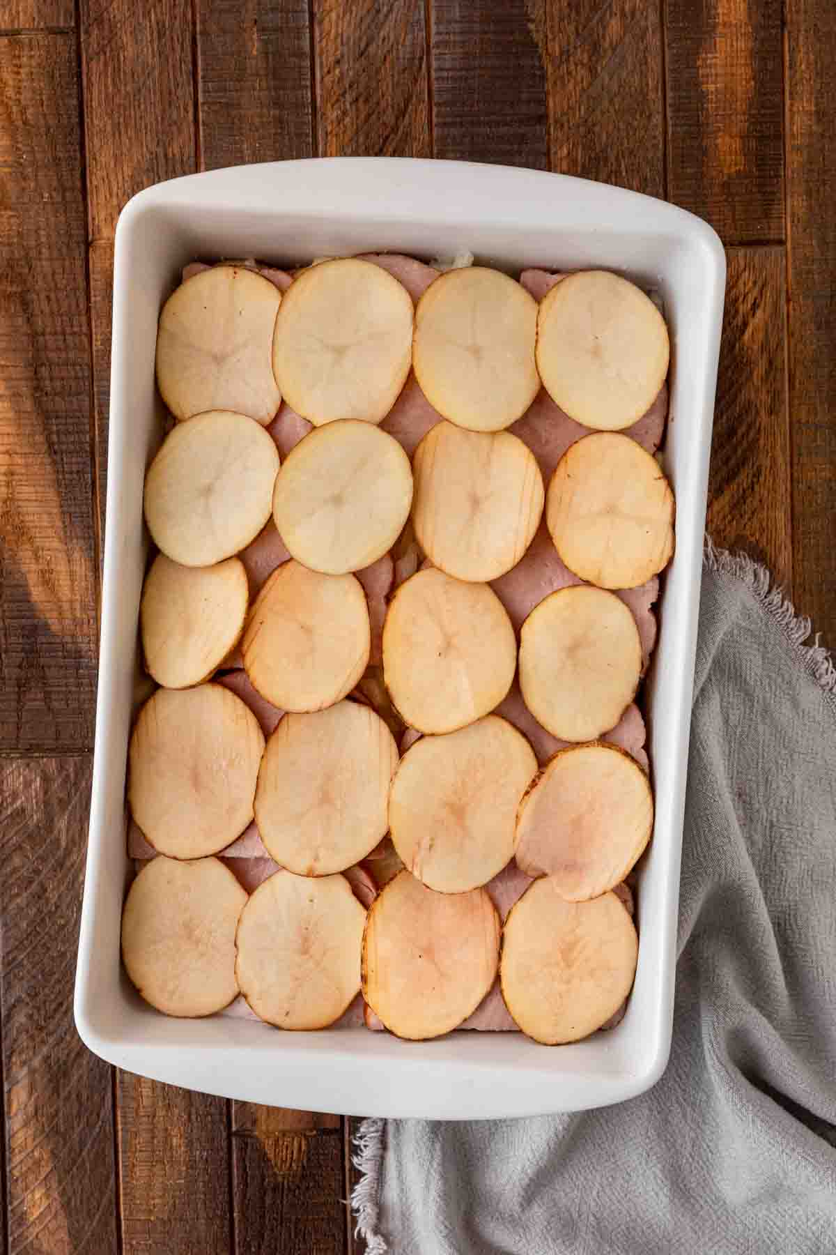 Scalloped Potatoes and Ham layer of potatoes added in baking dish