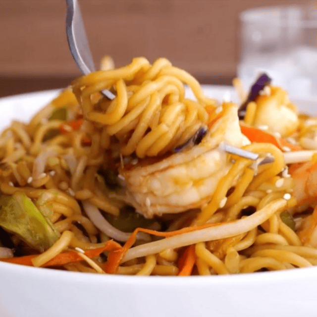 Bowl of noodles, veggies, and seafood with a fork ready to eat
