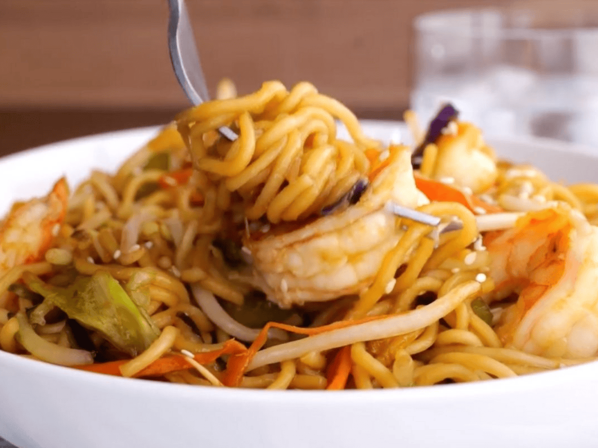 Bowl of noodles, veggies, and seafood with a fork ready to eat