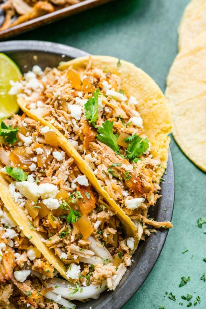 Slow Cooker Pork Carnitas three tacos on plate with cheese and cilantro