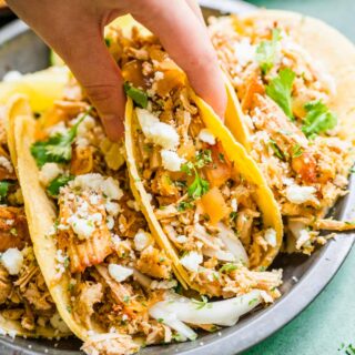 Slow Cooker Pork Carnitas three tacos with cheese and cilantro hand holding middle taco