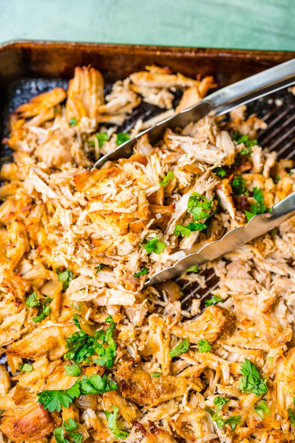 Slow Cooker Pork Carnitas shredded cooked meat on baking sheet after broiling with tongs