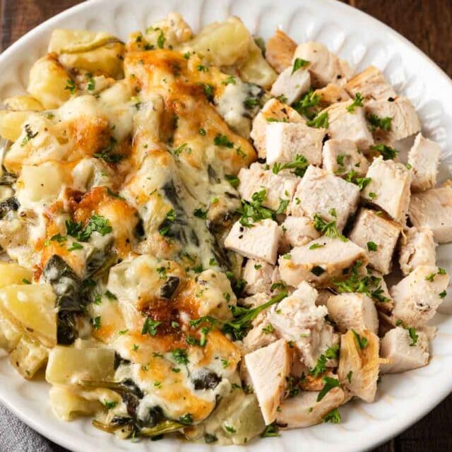 Creamy potato and spinach dish on dinner plate with chicken.
