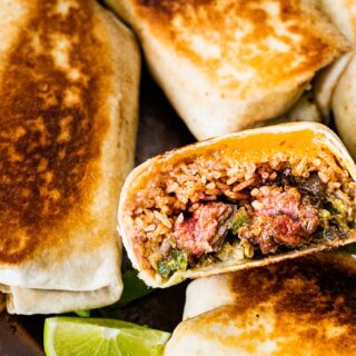 Cooked burritos on plate with 1 halved to see inside.