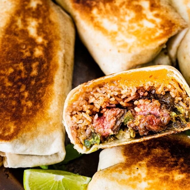 Cooked burritos on plate with 1 halved to see inside.