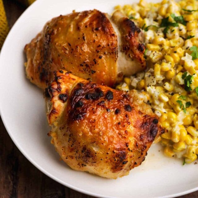 Baked Sweet and Spicy Honey Chicken two chicken thighs on a plate with corn