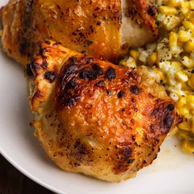 Baked Sweet and Spicy Honey Chicken two chicken thighs on a plate with corn