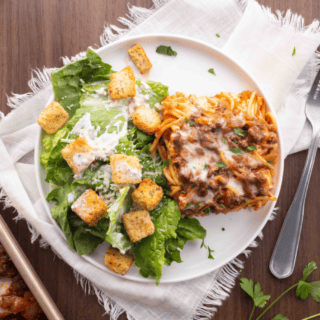 Baked pasta served on a plate with a side salad