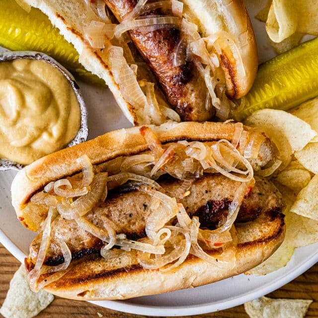 Grilled brats in bun with onion and mustard.