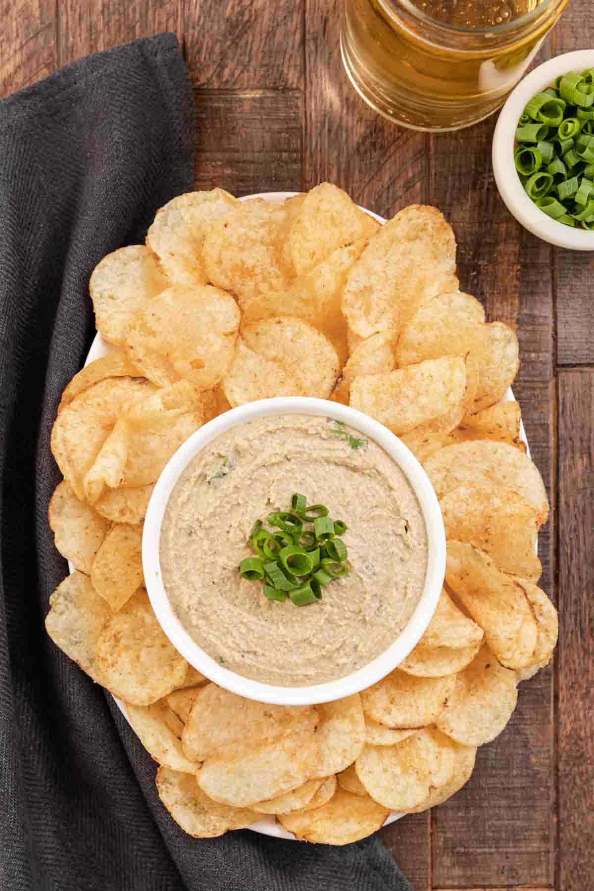 Clam Dip finished in bowl with green onions on top and bowl surrounded by potato chips on platter