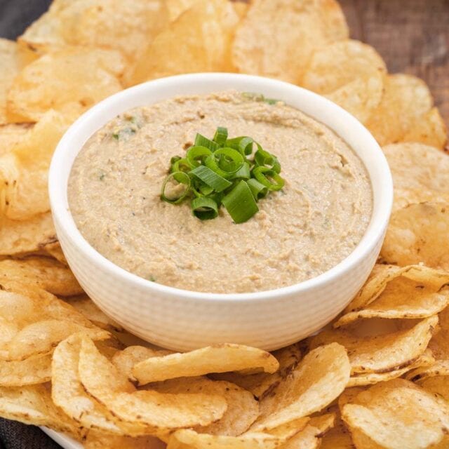 Dip finished in a bowl with green onions on top and bowl surrounded by potato chips on platter
