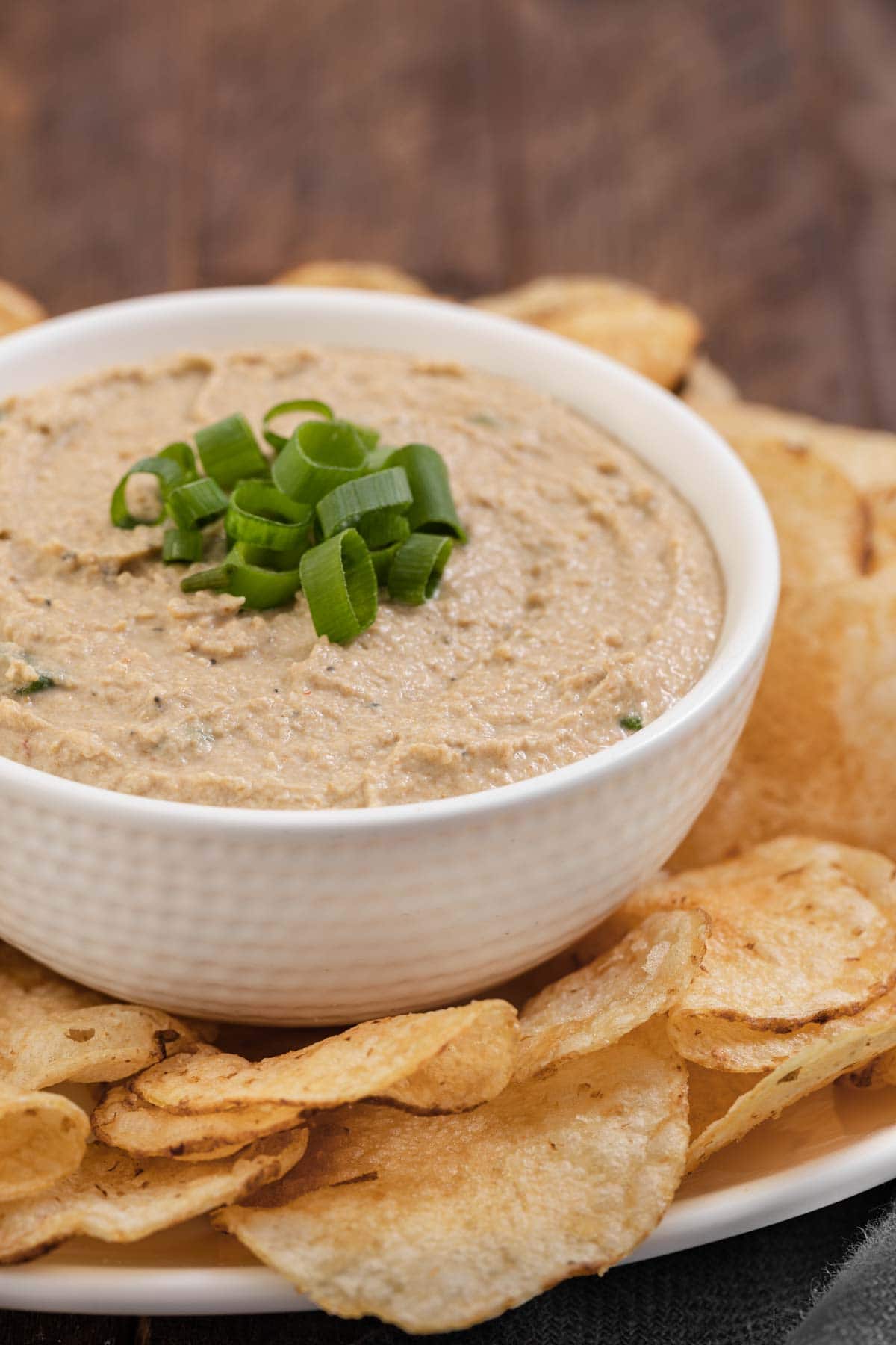 Clam Dip finished in bowl with green onions on top and bowl surrounded by potato chips on platter