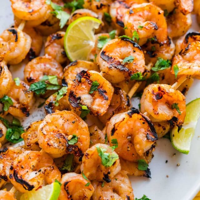plate of grilled shrimp on a skewer with lime wedges and cilantro garnish