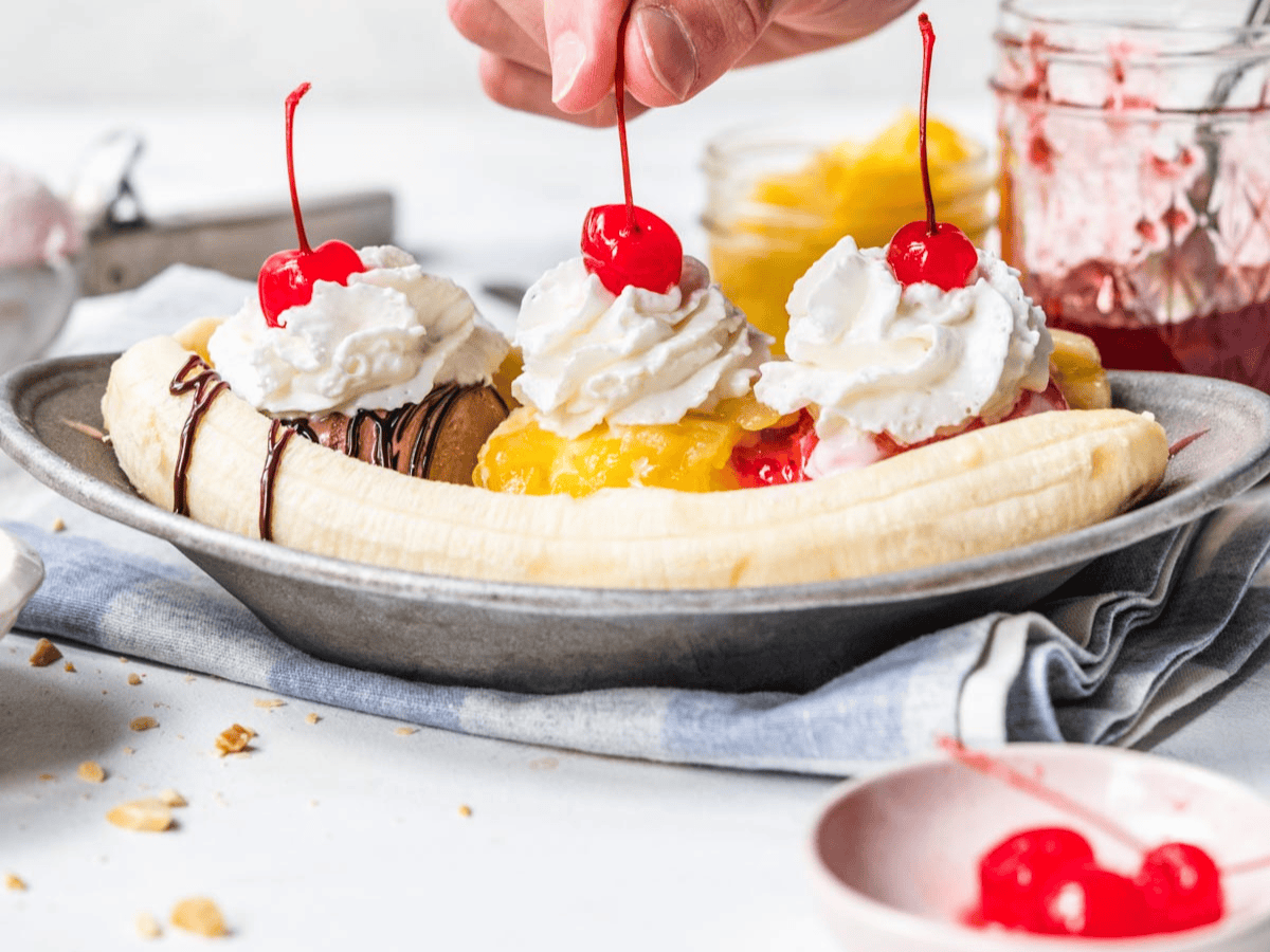 hand putting cherries on top of banana split 
