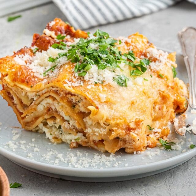 Large slice of cheesy lasagna on dinner plate.