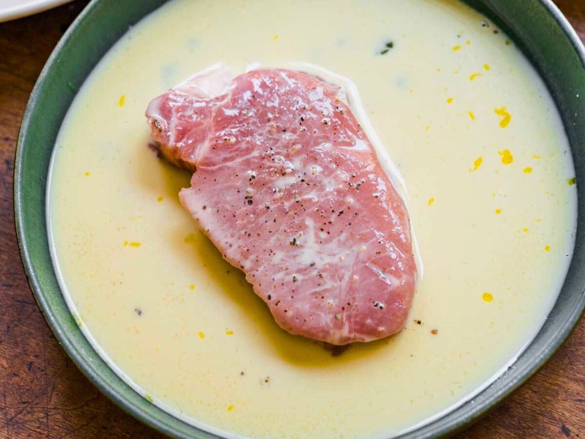 One raw pork chop in egg batter bowl.