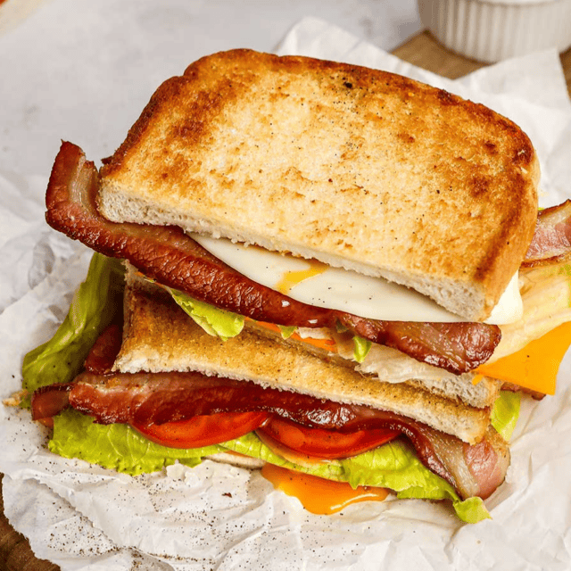 Assembled egg and bacon sandwich with lettuce and tomatoes.