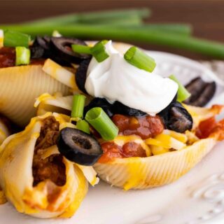 Cheesy Taco Stuffed Shells on dinner plate with sour cream, olives and green onion toppings