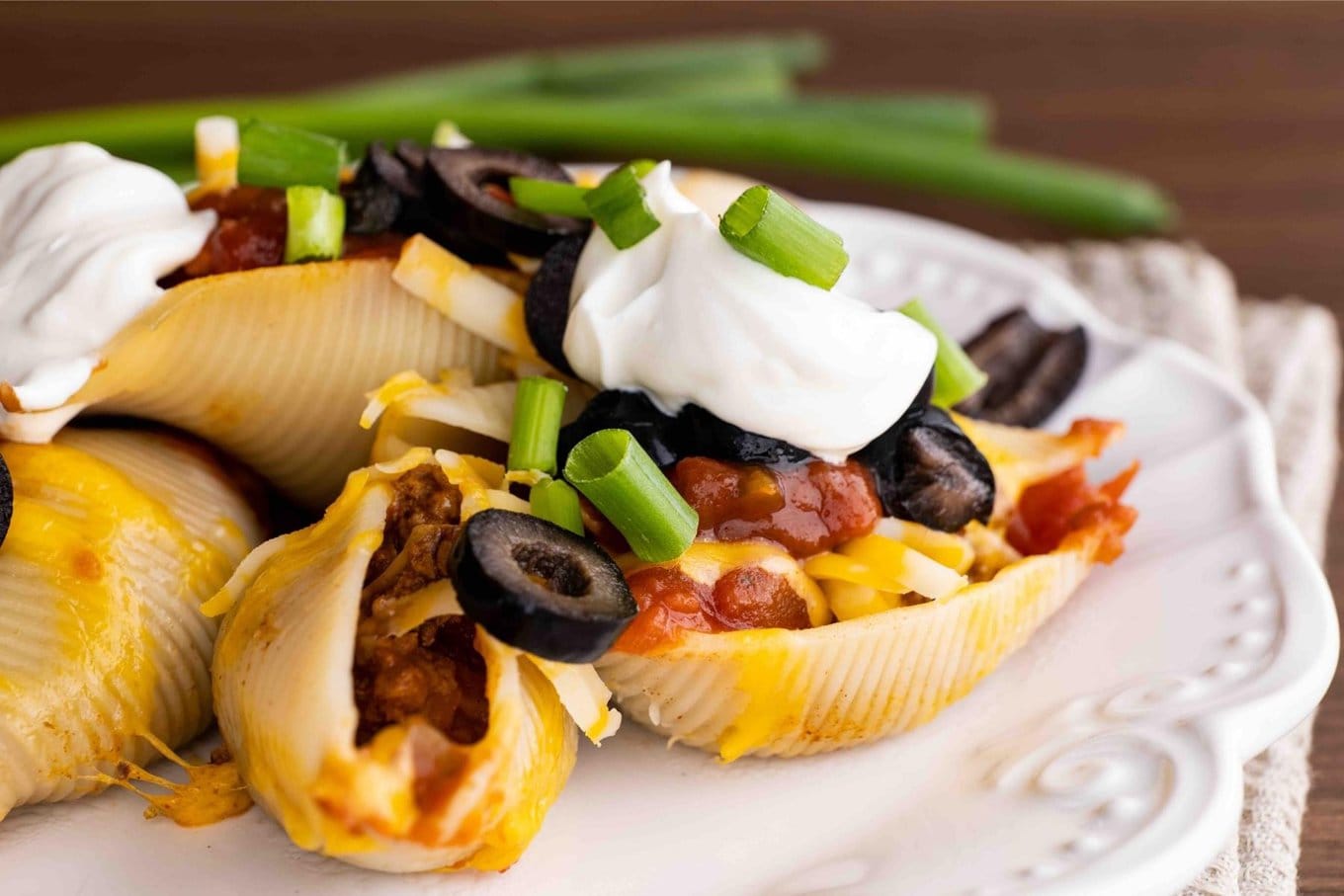 Cheesy Taco Stuffed Shells on dinner plate with sour cream, olives and green onion toppings