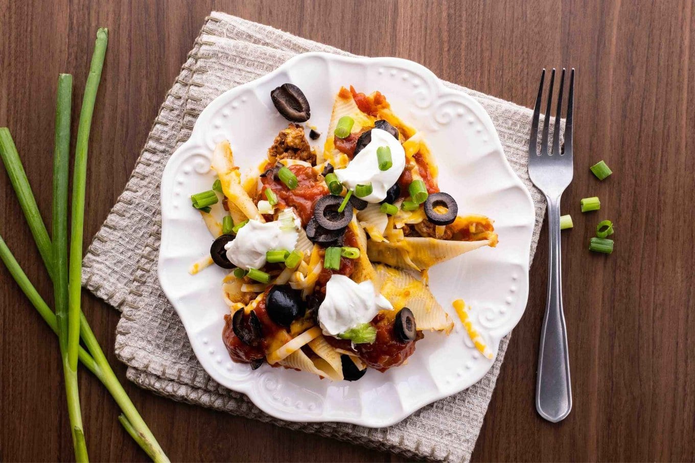 Cheesy Taco Stuffed Shells on dinner plate with sour cream, olives and green onion toppings