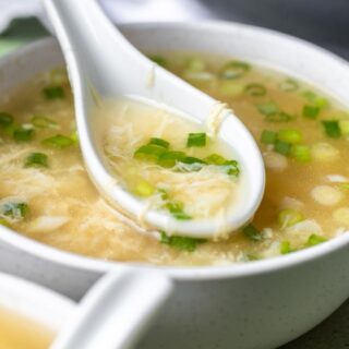 Chicken broth based soup in bowl with green onion, and ceramic spoon.
