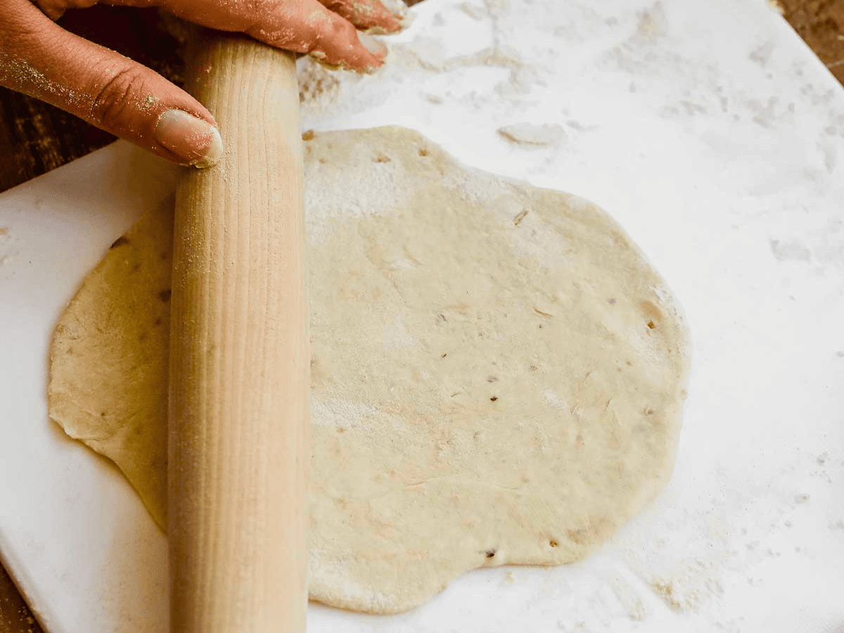 hands holding a rolling pin with dough on the table
