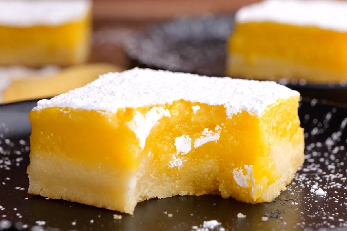 Lemon Bars square on plate with powdered sugar topping and bite taken