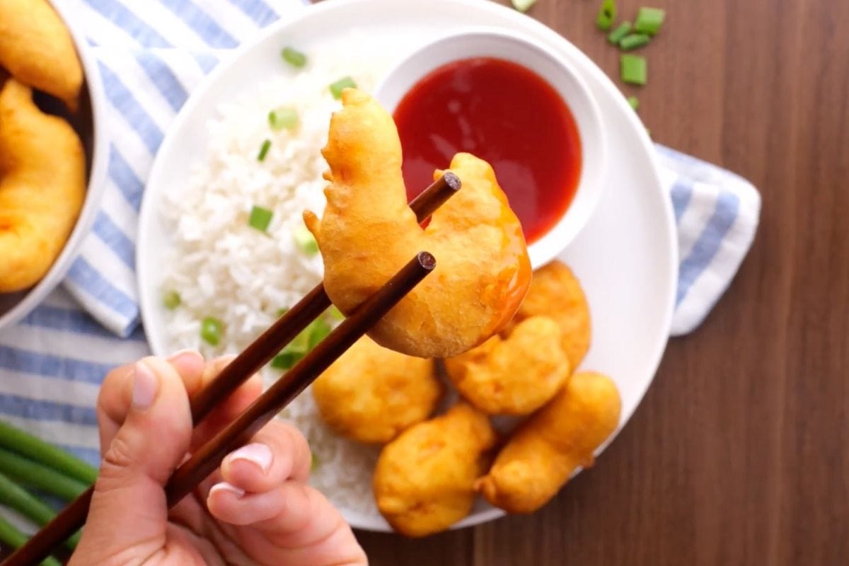 Shrimp Tempura in bowl with rice and sauce, chopstick holding piece