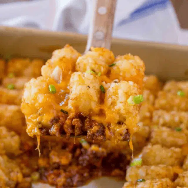 Spatula picking up beef and tater tot casserole with cheese.