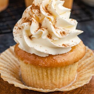 Decorated cupcake with wrapper pulled down on small wood plate