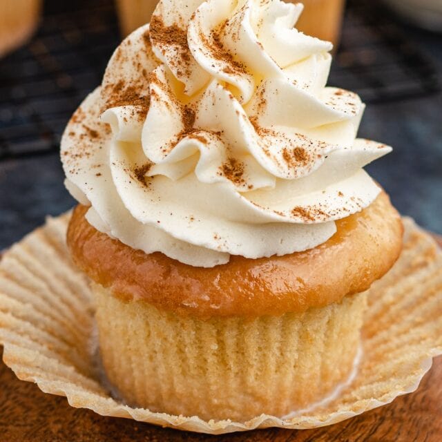Decorated cupcake with wrapper pulled down on small wood plate