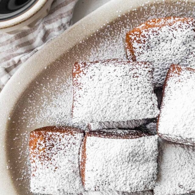 Pastries dusted in powdered sugar on a plate with coffee on the side