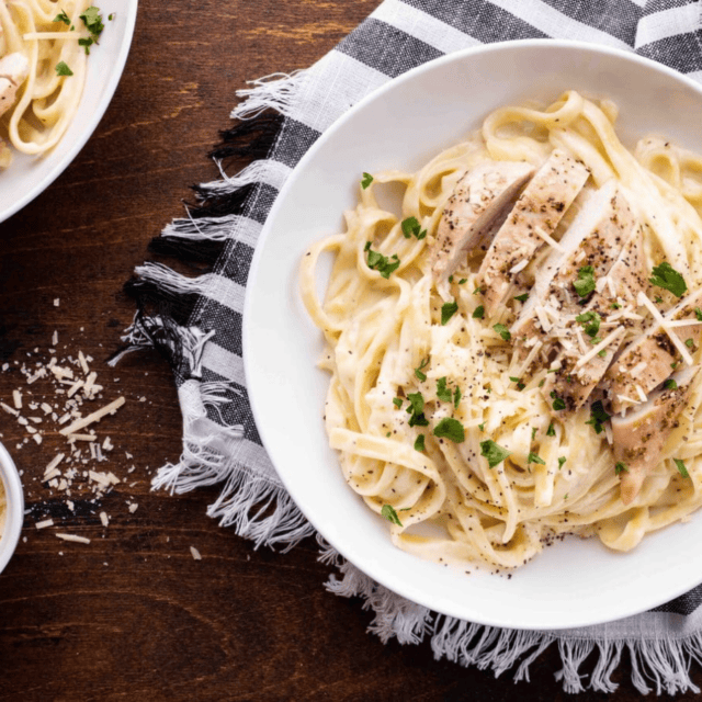 table with 2 plates of noodles and pasta topped with chicken