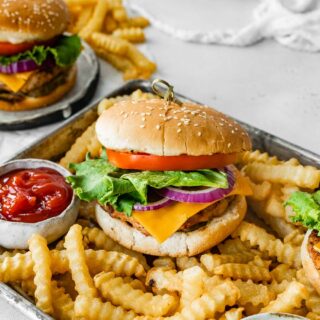 Assembled burgers with crinkle fries on metal tray with cup of ketchup