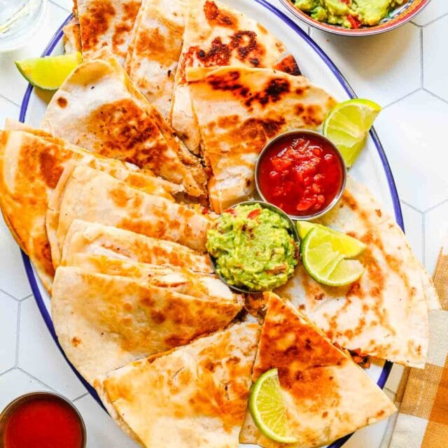 Chicken Quesadilla cooked and cut quesadilla wedges on plate with guacamole, lime wedges and salsa