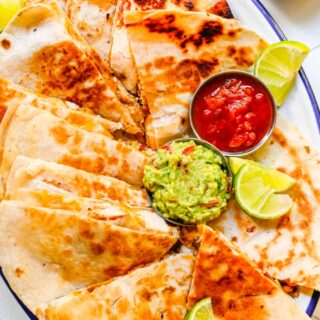 Cut quesadilla on plate with guacamole, lime wedges and salsa.