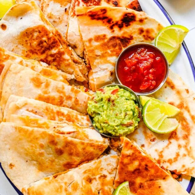 Cut quesadilla on plate with guacamole, lime wedges and salsa.